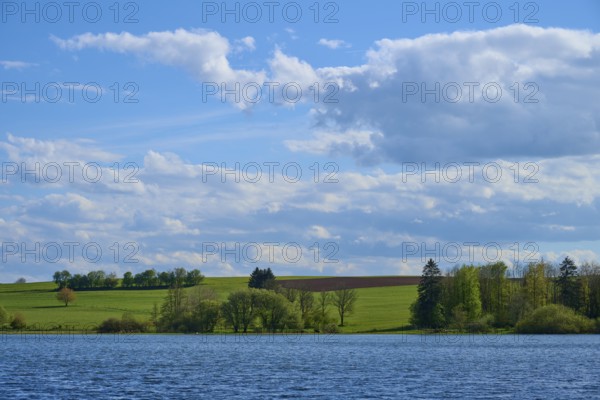 Ober- Moosersee surrounded by green fields and trees under a partly cloudy blue sky, spring, Freiensteinau, Vogelsberg, Hesse, Germany