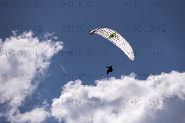 A person floats with a paraglider high in the sky in front of white clouds