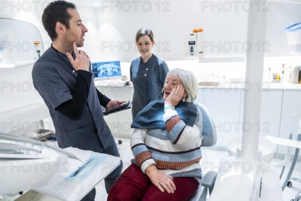 Senior woman suffering from toothache discussing treatment options with dentist and nurse in a modern dental clinic