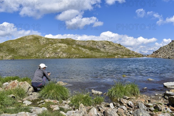 Woman photographing high alpine mountain lake at the Weiße Spitze, in the background the Großglockner, Deferegger Alps, Hohe Tauern, East Tyrol, Austria