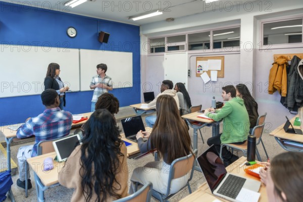 Multi ethnic group of high school students attending a lesson with two teachers and using laptops in a modern classroom