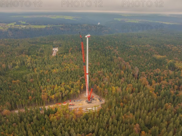 A tall crane erects a wind turbine in the dense autumn forest, wind farm construction site, Grömbach, Black Forest, Germany