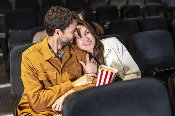 Romantic couple enjoying a movie night, sharing popcorn and affection in a comfortable cinema seat