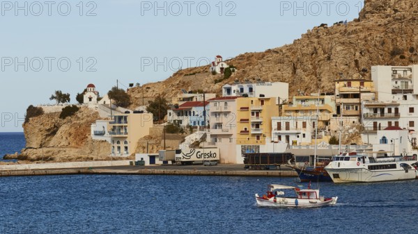 A coast with boats, colourful houses on rocks, surrounded by deep blue sea and a harbour, fishing boat leaving harbour, Pigadia, town and harbour, Pigadia Bay, main town, Karpathos, Dodecanese, Greek Islands, Greece