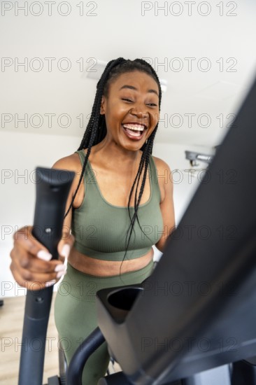 Cheerful black woman enjoys her workout on an elliptical trainer, maintaining her fitness routine while traveling
