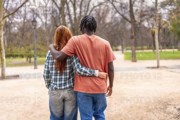 Young multi ethnic couple walking together in a park with arms around each other, enjoying a romantic stroll