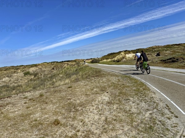 Cyclist on a wide cycle path through a dune landscape under a blue sky with clouds, north sea Cyle route, Scheveningen, Netherlands