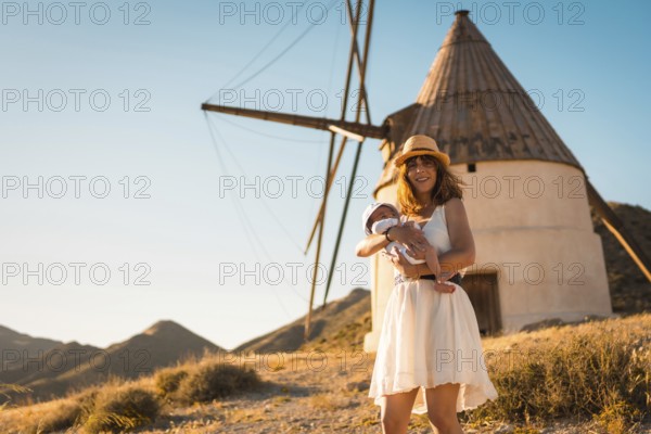 Mother holding a newborn baby next to a windmill in Cabo de Gata, Spain