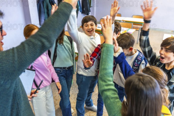 Group of cheerful elementary school students and teacher raising hands together in classroom, celebrating success and teamwork