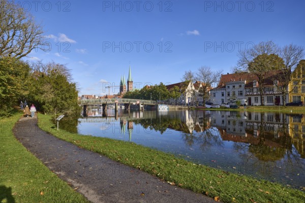 River Trave at high water, general architecture, footpath, pedestrian bridge, trees and bushes, reflections on the water surface, blue sky with fair weather clouds, Hanseatic city of Lübeck, independent city, Schleswig-Holstein, Germany