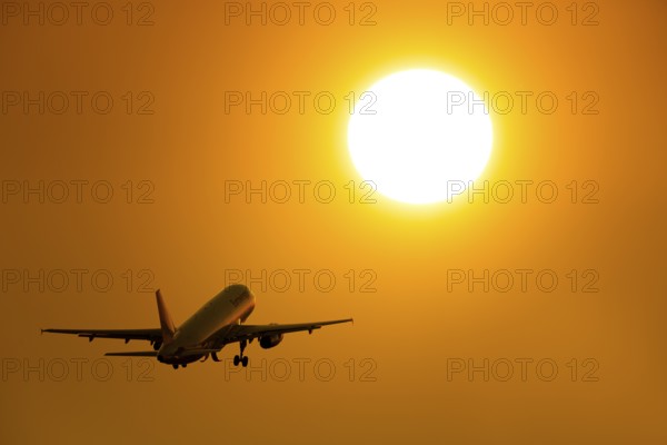 Silhouette of an aircraft taking off in front of a bright orange sunset