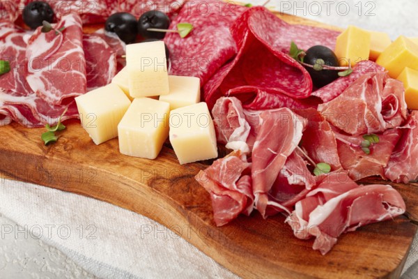 Assorted, sliced meat appetizer, prosciutto, salami and ham, with cheese and olives, on a wooden board, breakfast, top view, close-up, no people