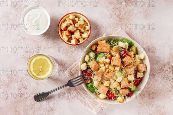 Caesar salad with salmon, with croutons and dressing, in a salad bowl, on a pink table