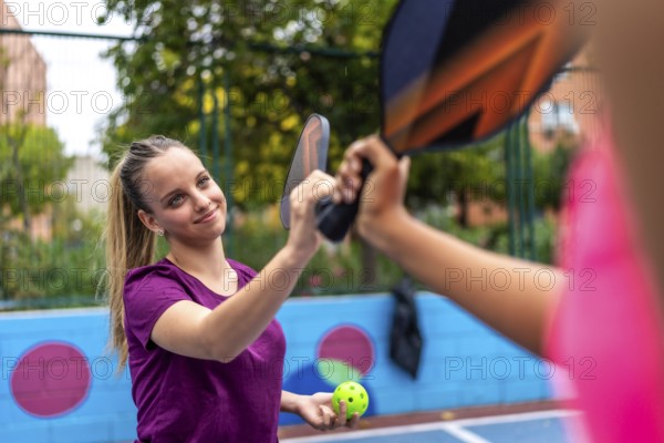 Smiling sportive blonde woman shaking racket with partner in a pickelball court