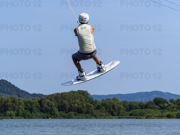 Young man jumping with wakeboard over jump and obstacle, water sports, water skiing in wakepark, Stráž pod Ralskem, Czech Republic