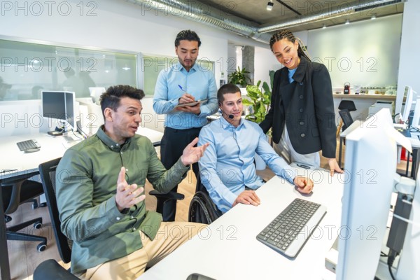 Diverse business team collaborating on a computer project, demonstrating inclusion and teamwork in the workplace with a disabled colleague in a wheelchair