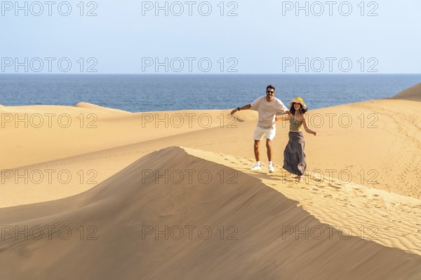 Couple running down sand dunes at maspalomas with ocean in background enjoying summer vacation in gran canaria