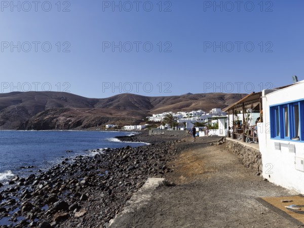 Black lava beach, white houses, fish restaurant, coastline, fishing village Playa Quemada, Yaiza, Lanzarote, Spain