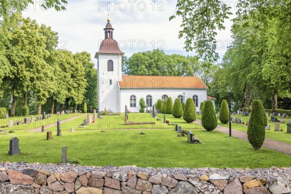 Church with tombstones in the Swedish countryside with lush green trees a summer day, Kättilstorp, Sweden