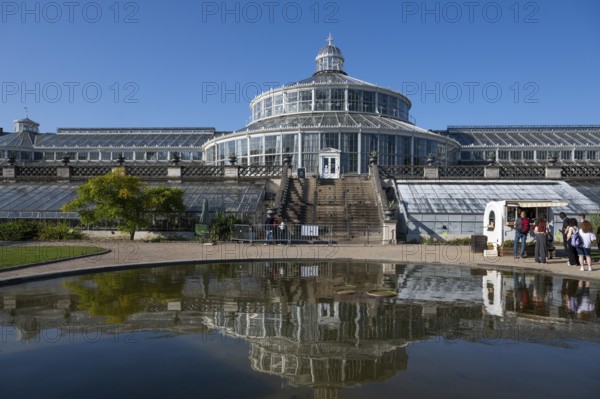 Large historic greenhouse reflected in a pond, palm house with glass facade, blue sky, Botanical Garden or Botanisk Have, University, Copenhagen, Denmark