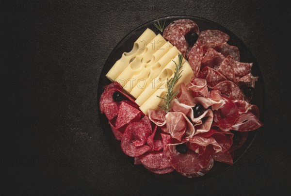 Cold cuts, appetizer, prosciutto, salami and ham, with maasdam cheese and olives, on a round plate, breakfast, top view, close-up, deserted