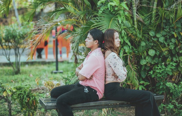 Upset young couple sitting back to back on a bench. Unhappy couple arguing on a public bench. Concept of couple problems and crisis