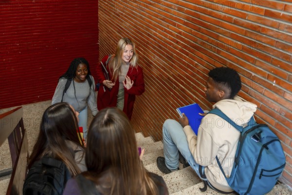 Multi ethnic students walking down the stairs and greeting a classmate sitting on the steps