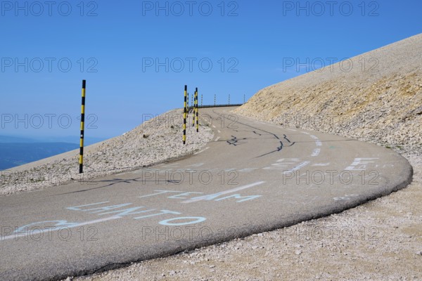 Winding road on a barren hill under a clear blue sky with yellow posts at the edge, Mont Ventoux, Vaucluse department, Provence, France