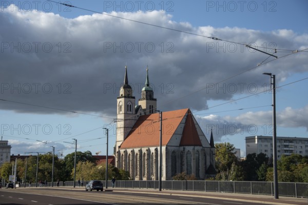 Close-up of St John's Church with two towers and red roof, next to a street and under a sky with clouds, Magdeburg, Saxony-Anhalt, Germany