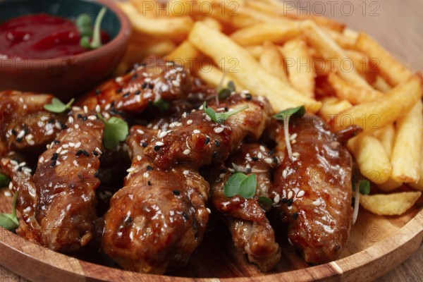 Barbecue chicken wings, sprinkled with sesame seeds, with French fries, and sauce, on a wooden plate, rustic style