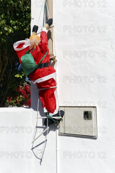 Artificial Father Christmas with rucksack, climbs up ladder, white house facade, funny decoration, Haria, Lanzarote, Canary Islands, Spain