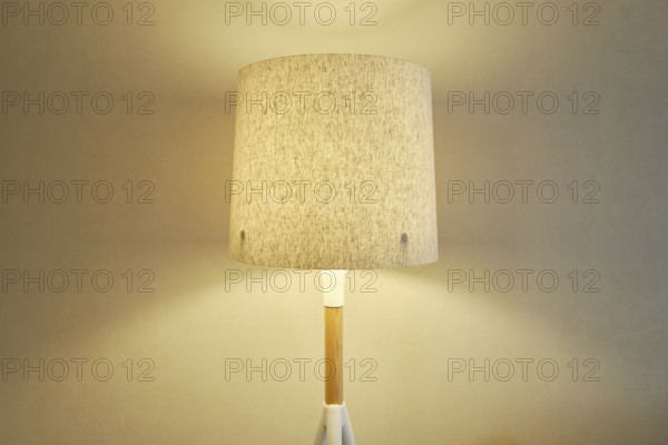 A stylish lamp with a beige fabric shade casting a soft warm light on the wall in the room