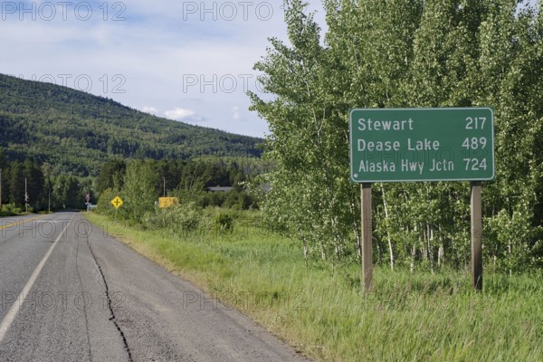 Narrow, traffic-free road leads through forest landscape, sign with huge distances, wilderness, Stewart Cassiar Highway, British Columbia, Canada