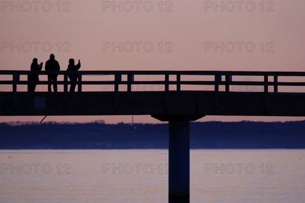 Holidaymaker with mobile phone at sunset on the pier Sellin, Mecklenburg-Vorpommern, Germany