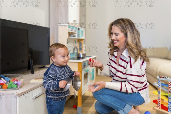 Happy mother and baby boy playing with toy kitchen set in living room, enjoying quality time together