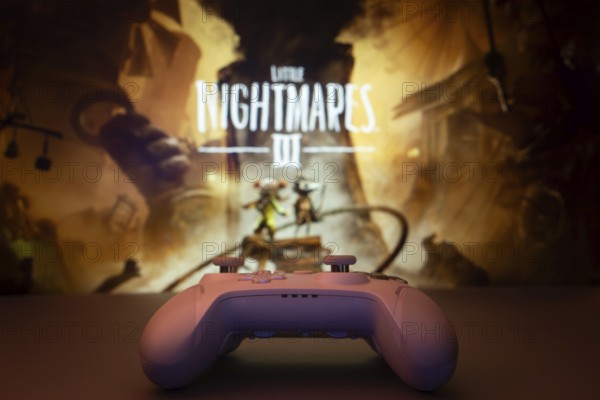 Dhaka, Bangladesh- 22 July 2025: A close-up of a gamepad with the little nightmares 3 seen on screen in the background. Little Nightmares III is an upcoming horror adventure video game