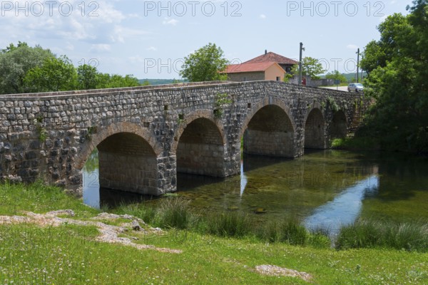 Stone bridge over river, flanked by green bank and small building, Bridge over the river Zrmanja, Žegar, Zegar, Zadar, Croatia