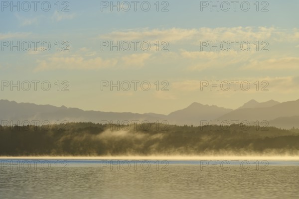 Fog over a calm lake under a clear sky with mountains in the background, Lake Mahinapua, Ruatapu, South Island, New Zealand