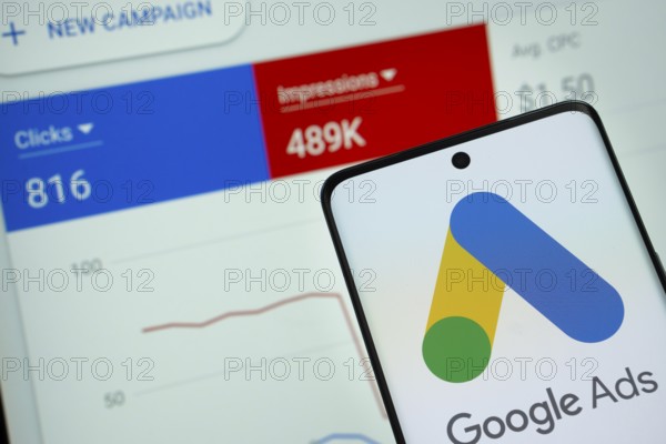 Google Ads logo is displayed on a smartphone screen, with a stock graph webpage visible on a computer screen in the background