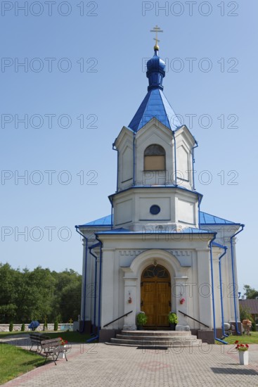 A small white Orthodox church with a blue roof stands in sunny weather against a green backdrop, Orthodox Church of the Assumption of the Virgin Mary, Dubiny, Podlaskie Voivodeship, Podlaskie, Poland