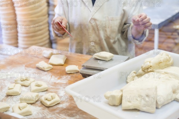 Woman bread maker employee in artisan bakery workshop cutting dough for hamburgers