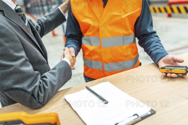 Manager and warehouse worker shaking hands after signing a contract in a logistics center