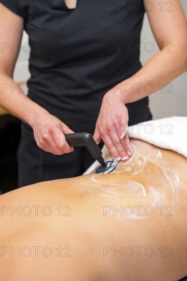 Vertical close-up photo of an unrecognizable massage therapist using the INDIBA machine to relieve back pain in a woman