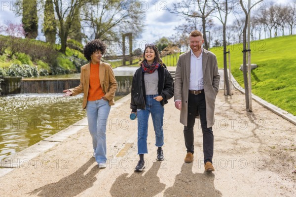 Three young professionals enjoy a walk and talk together during their lunch break in a sunny city park