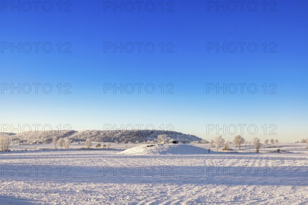 Winter landscape with snow and frost in the countryside with a Passage grave on a hill and a table mountain Ålleberg that is part of the Swedish Unesco geopark Falköping, Karleby, Sweden