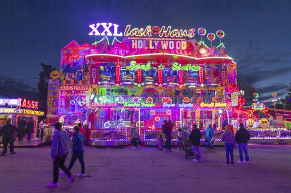 Colourfully illuminated fun house at a funfair at night with numerous visitors, Cannstatter Wasen, folk festival, Bad Cannstatt, Stuttgart, Baden-Württemberg, Germany