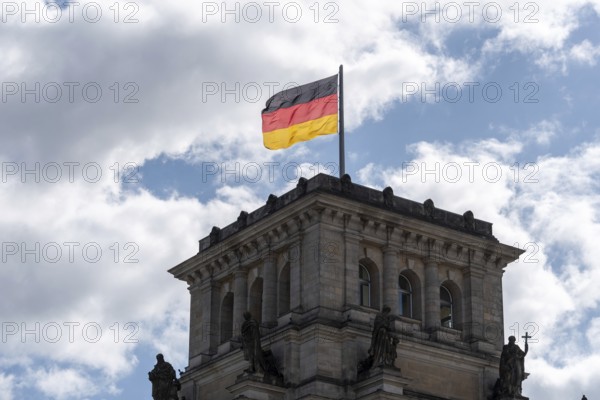 A German flag flies over a building tower of the Reichstag against a cloudy sky, Berlin, Germany