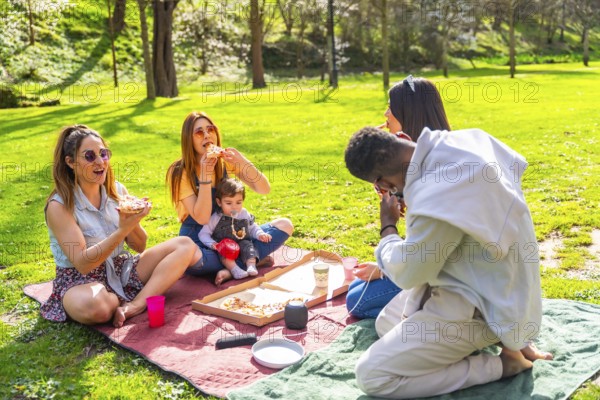 Group of friends savoring delicious pizza while enjoying a sunny picnic in a vibrant park, surrounded by laughter and good company