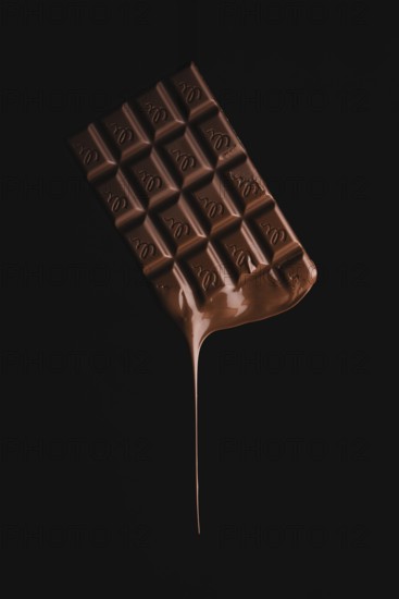 A floating chocolate bar with melting drops on a black background