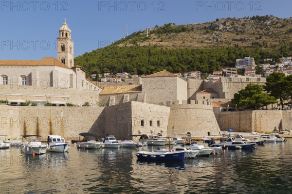 Old walled city of Dubrovnik with Dominican Monastery bell tower and Zrinski sightseeing tour boat moored in harbour plus Mount Srd in the background in late summer, Croatia